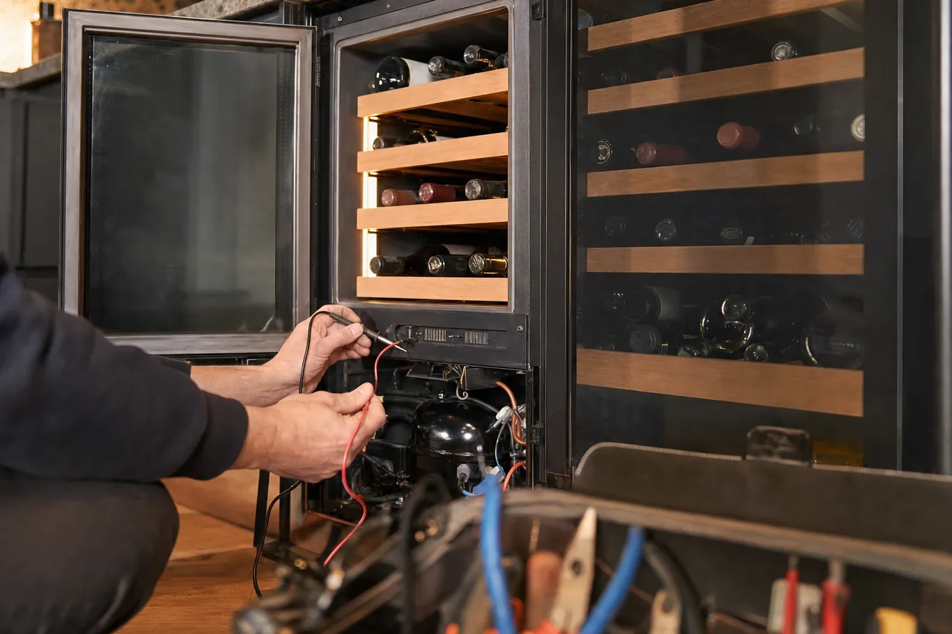 Glass-door wine storage with bottles on wooden racks, one door open and multimeter probes at the lower panel